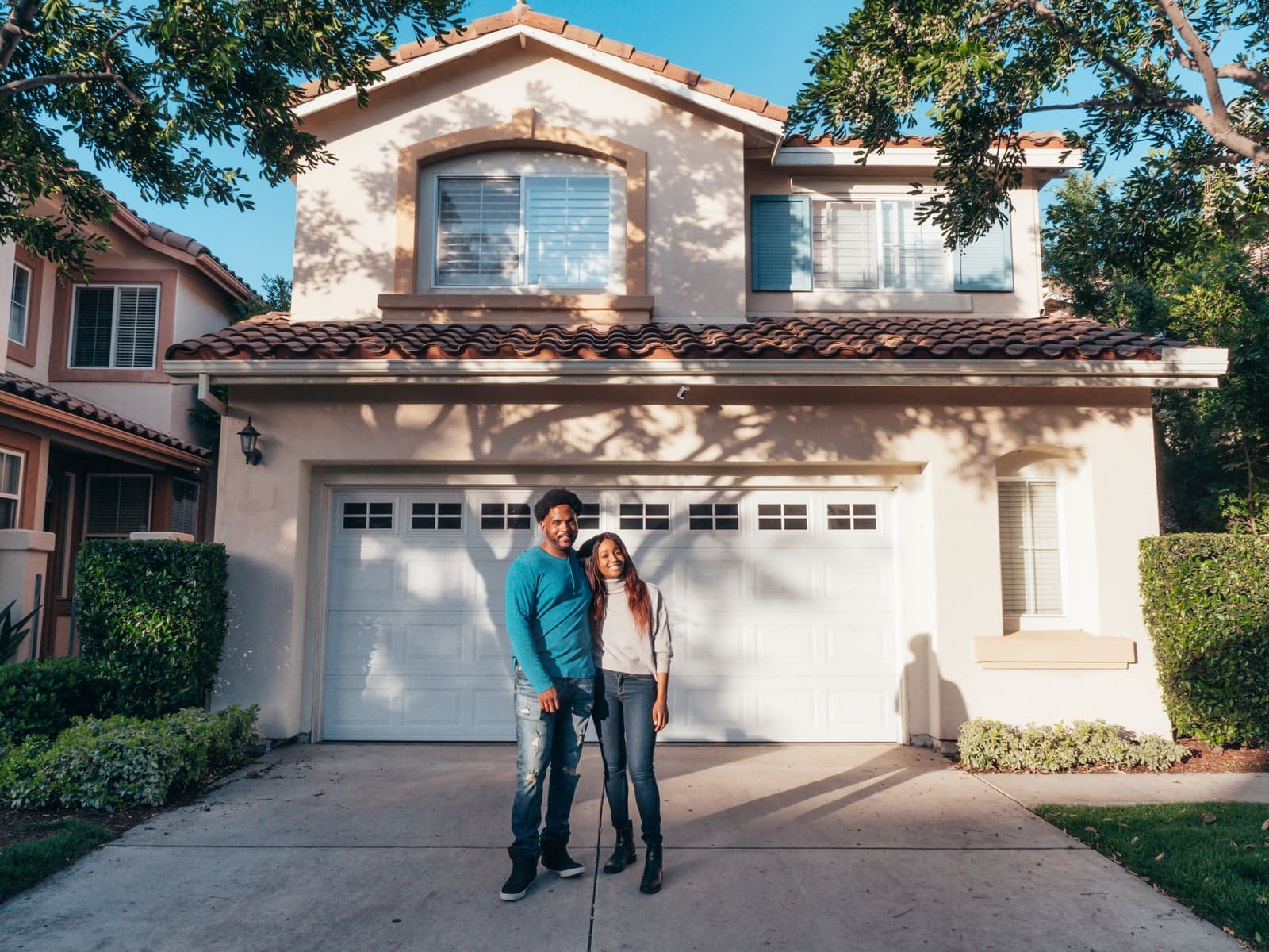 A couple standing together outside their home in late afternoon light
